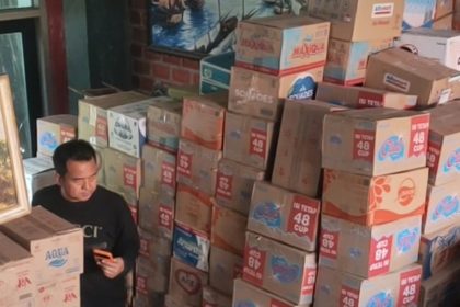 Cak Sholeh berada di tengah tumpukan duz air mineral dalam kemasan hasil donasi masyarakat. (foto: jero)